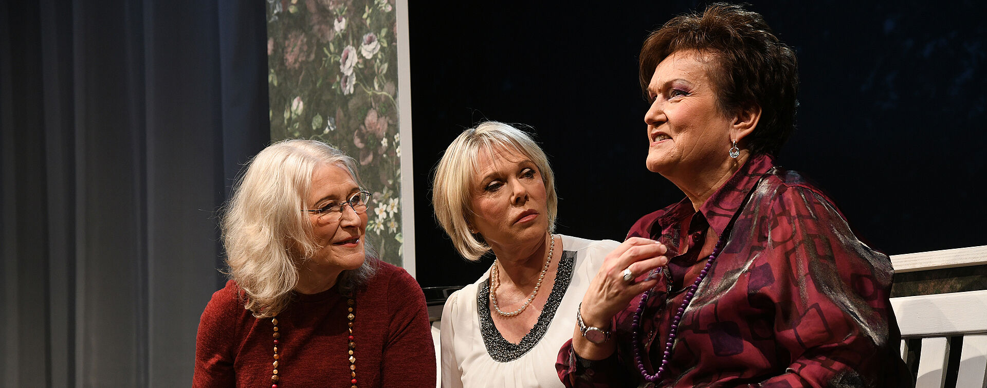 Drei Frauen sitzen auf der Bank, trinken Kaffee und sprechen miteinander.