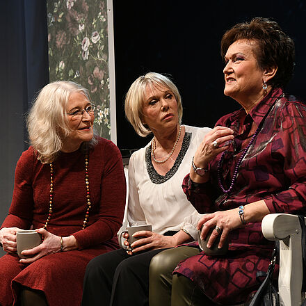 Drei Frauen sitzen auf der Bank, trinken Kaffee und sprechen miteinander.