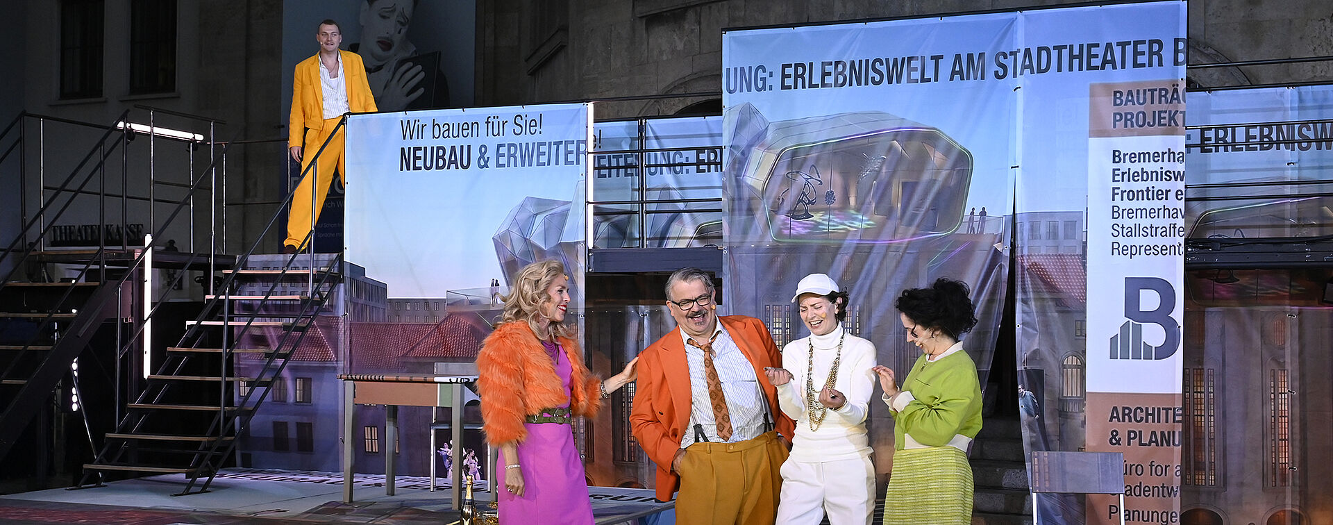 Vier Personen stehen vor einem Gerüst. Sie lachen.