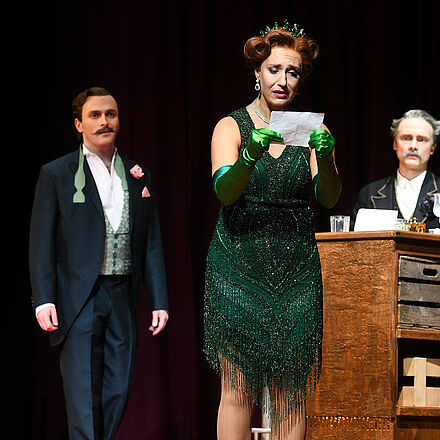 Eine Frau hält einen Brief in der Hand. Sie steht mit mehreren Männern an einer Bar.