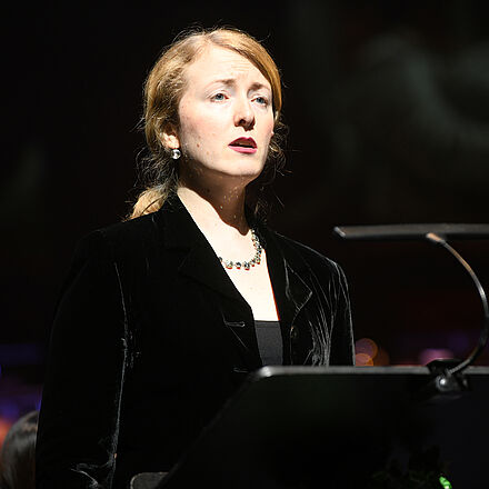 Eine Person steht an einem Notenständer und singt.  