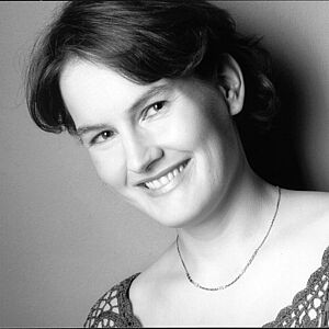 Schwarzweißes Portraitfoto von Brigitte Rickmann. Die Platzierung des Fotos ist leicht schräg. Sie blickt mit geneigtem Kopf in die Kamera. Ihr kurzes Haar fällt ihr hinter die Ohren. Sie grinst mit geöffnetem Mund. Sie trägt eine dezente kurze Halskette, die ihr auf der Haut liegt. Sie trägt ein gehäkeltes Oberteil.
