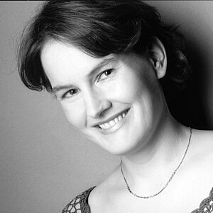 Schwarzweißes Portraitfoto von Brigitte Rickmann. Die Platzierung des Fotos ist leicht schräg. Sie blickt mit geneigtem Kopf in die Kamera. Ihr kurzes Haar fällt ihr hinter die Ohren. Sie grinst mit geöffnetem Mund. Sie trägt eine dezente kurze Halskette, die ihr auf der Haut liegt. Sie trägt ein gehäkeltes Oberteil.