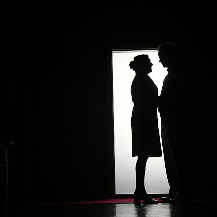 Im Hintergrund sieht man Licht in Form einer Tür. Vor dem Licht stehen zwei Schattenfiguren.