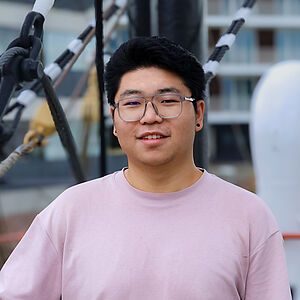 Portrait eines jungen asiatischen Mannes mit Brille und lila Pullover