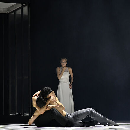 Tänzer:innen umarmen sich. Im Hintergrund steht eine Tänzerin.