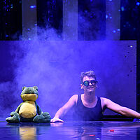 Ein Frosch und Einaug schauen aus einer Kiste im Boden hervor