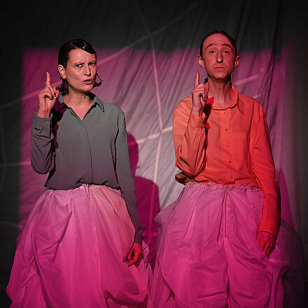 Das Licht ist rosa. Zwei Personen zeigen mit dem Zeigefinger.