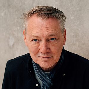 Portraitfoto von Dirk Böhling. Er hat graues kurzes Haar, trägt einen blauen Schal und ein dunkelblaues Hemd.