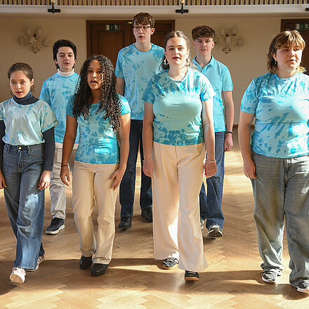 Vier Mädchen und drei Jungen im blauen Oberteil stehen im Mittelpunkt des Bildes.