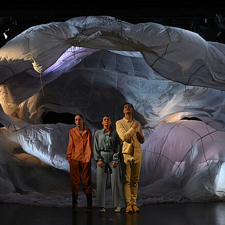 Stoff fällt von der Bühne. Drei Personen stehen davor.