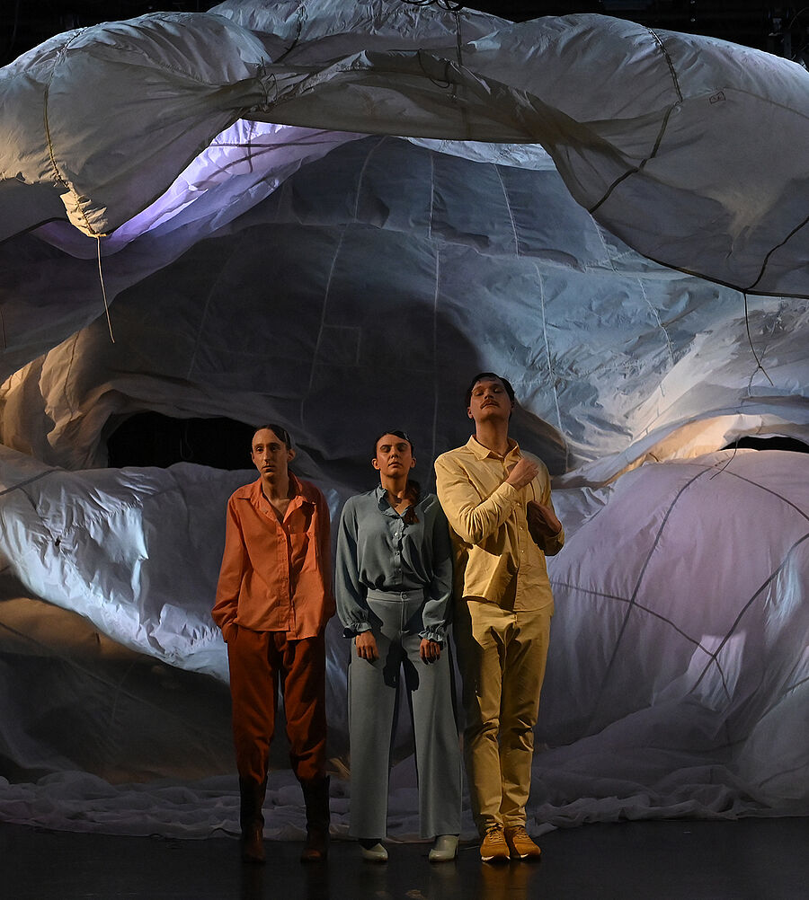 Stoff fällt von der Bühne. Drei Personen stehen davor.