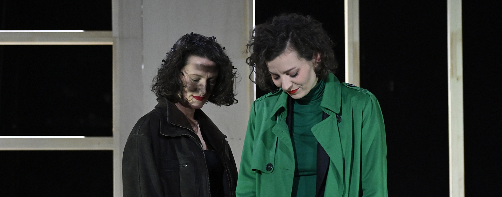 Die Frau steht neben der Frau im grünen Anzug. Beide schauen zu Boden.