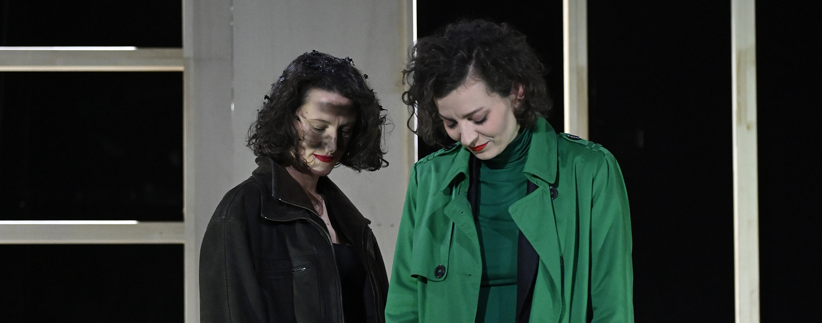 Die Frau steht neben der Frau im grünen Anzug. Beide schauen zu Boden.