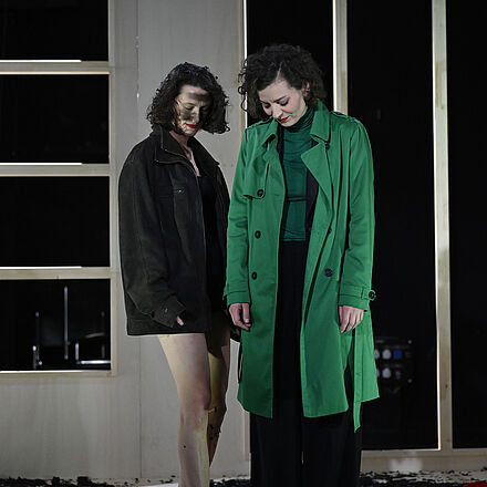 Die Frau steht neben der Frau im grünen Anzug. Beide schauen zu Boden.