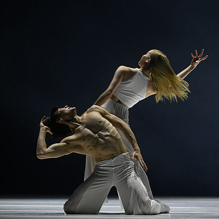 Eine Tänzerin steht mit dem Rücken zur Kamera. Vor ihr kniet ein Tänzer.