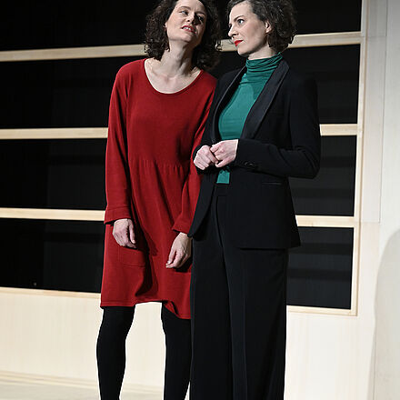 Eine Frau im roten Kleid und eine Frau im Anzug stehen nebeneinander.