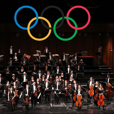 Das Philharmonische Orchester Bremerhaven im Großen Haus auf der Bühne. Über ihnen die Olympischen Ringe.