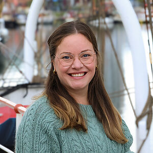 Portrait einer lächelnden jungen Frau mit Brille und grünem Pullover