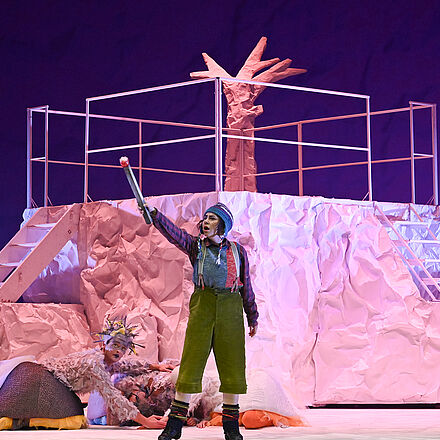 Die kleine Person hält ein Streichholz in der Hand. Hinter ihr liegen mehrere Gänse