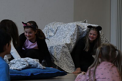 Zwei als Mäuse verkleidete Mädchen sitzen grinsend vor einer Kissenburg.