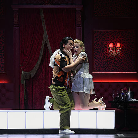 Ein Mann und eine Frau knien in der Mitte des Bildes auf einem Podest und halten sich in den Armen.