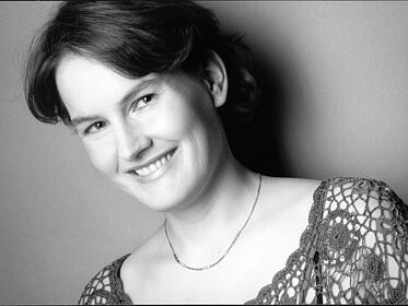 Schwarzweißes Portraitfoto von Brigitte Rickmann. Die Platzierung des Fotos ist leicht schräg. Sie blickt mit geneigtem Kopf in die Kamera. Ihr kurzes Haar fällt ihr hinter die Ohren. Sie grinst mit geöffnetem Mund. Sie trägt eine dezente kurze Halskette, die ihr auf der Haut liegt. Sie trägt ein gehäkeltes Oberteil.